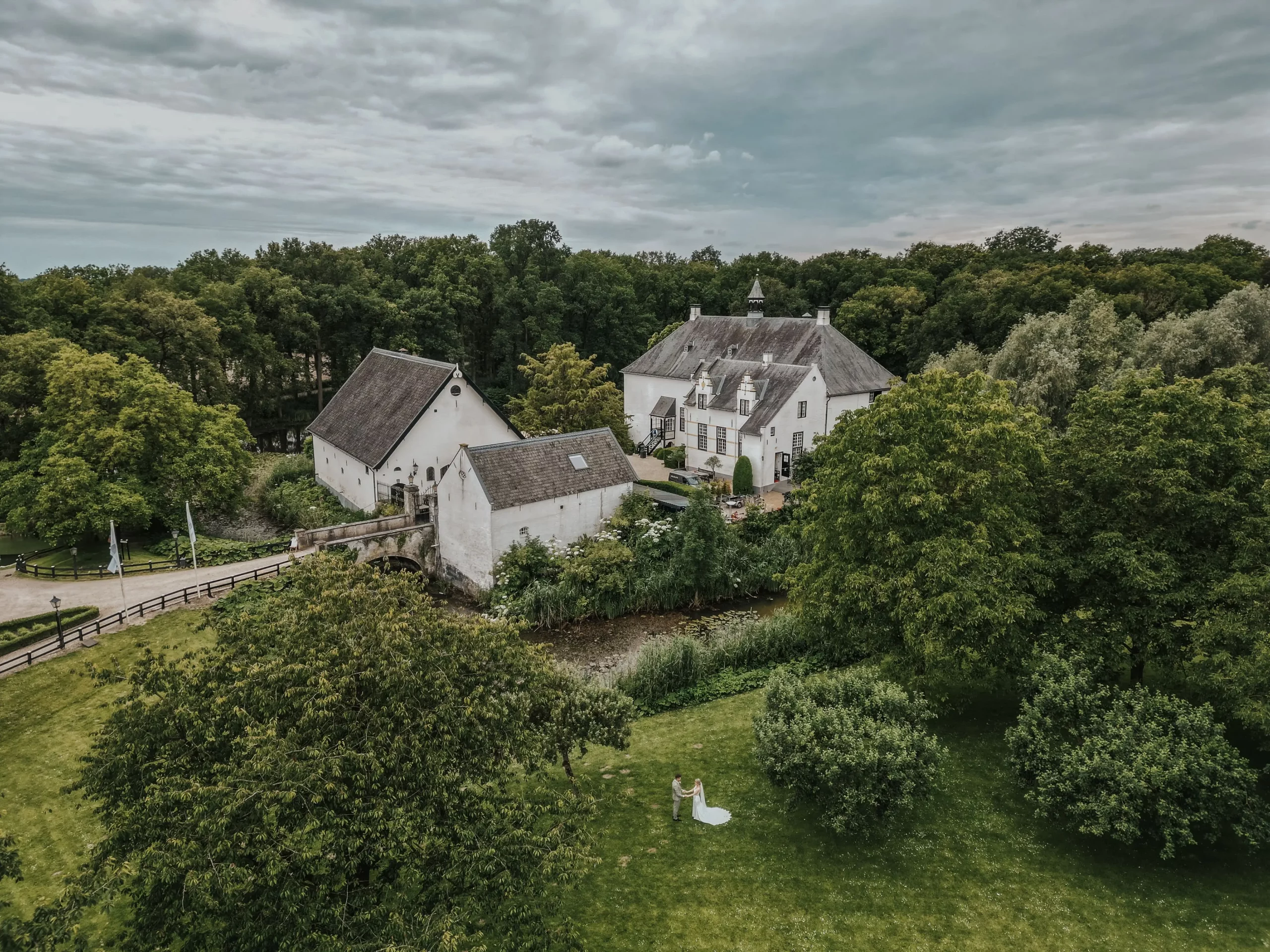 Luchtfoto van witte gebouwen met donkere daken, omringd door bomen en een grasveld